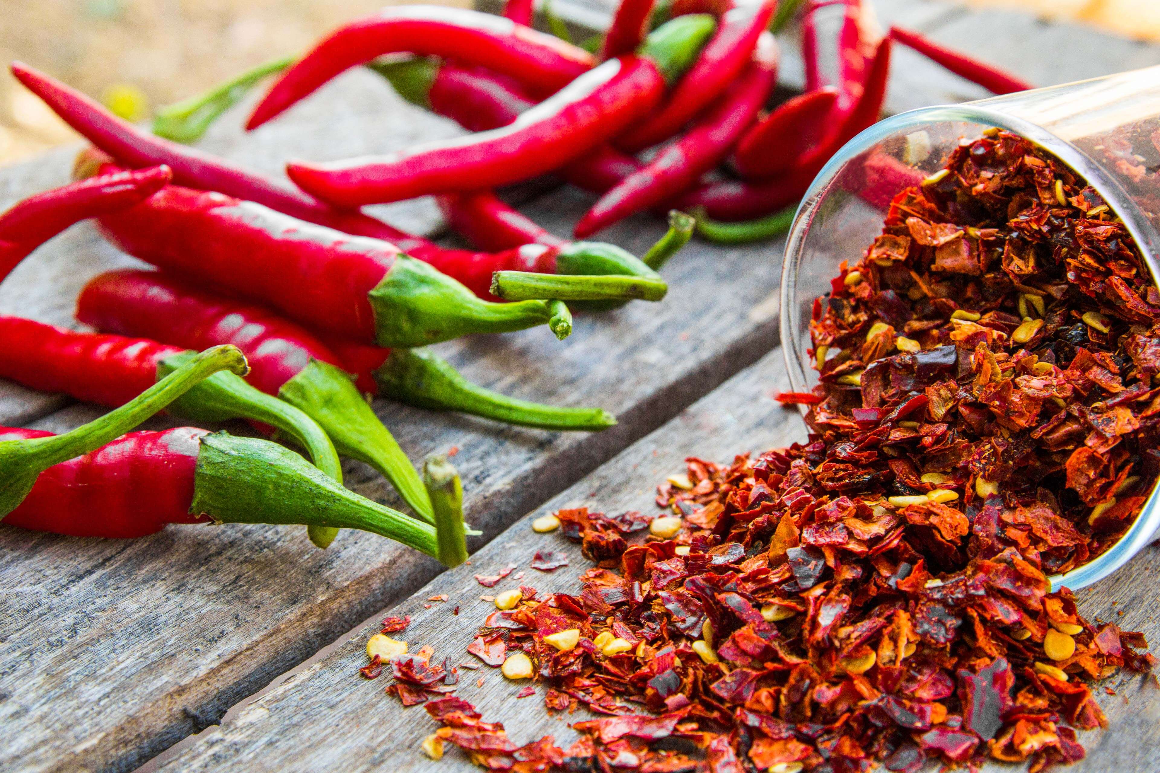 Frische rote Chilischoten neben einer Schale mit zerstoßenen roten Chiliflocken.