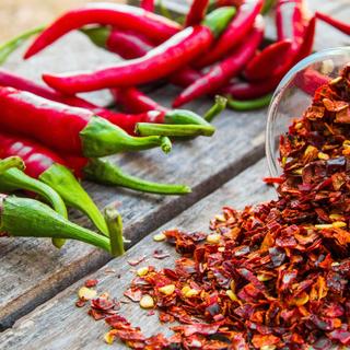 Frische rote Chilischoten neben einer Schale mit zerstoßenen roten Chiliflocken.