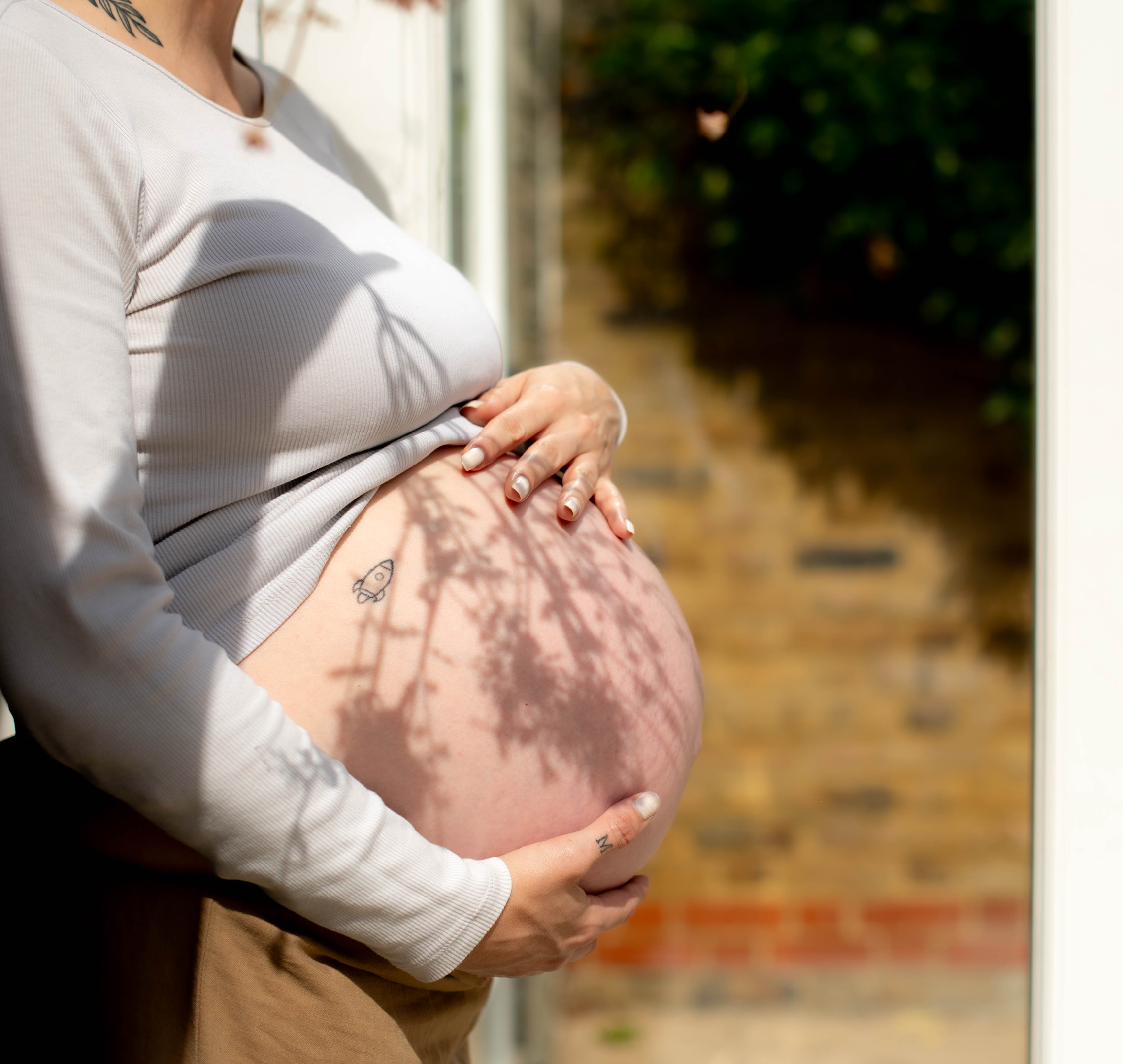 Pregnant woman gently holding her bare bump in soft sunlight, preparing for labour and birth