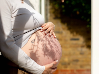 Pregnant woman gently holding her bare bump in soft sunlight, preparing for labour and birth
