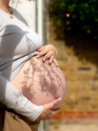 Pregnant woman gently holding her bare bump in soft sunlight, preparing for labour and birth