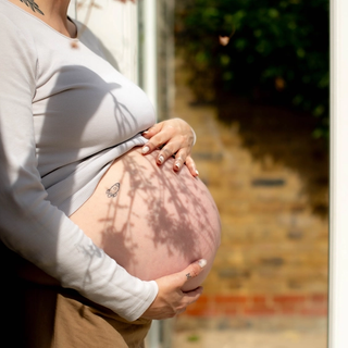 Pregnant woman gently holding her bare bump in soft sunlight, preparing for labour and birth