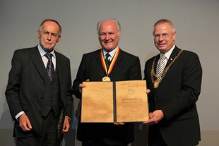 Drei festlich gekleidete Männer bei der Verleihung des Umweltschutzpreises „Goldene Blume von Rheydt“, der Geehrte hält Urkunde und Medaille.