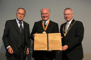 Drei festlich gekleidete Männer bei der Verleihung des Umweltschutzpreises „Goldene Blume von Rheydt“, der Geehrte hält Urkunde und Medaille.