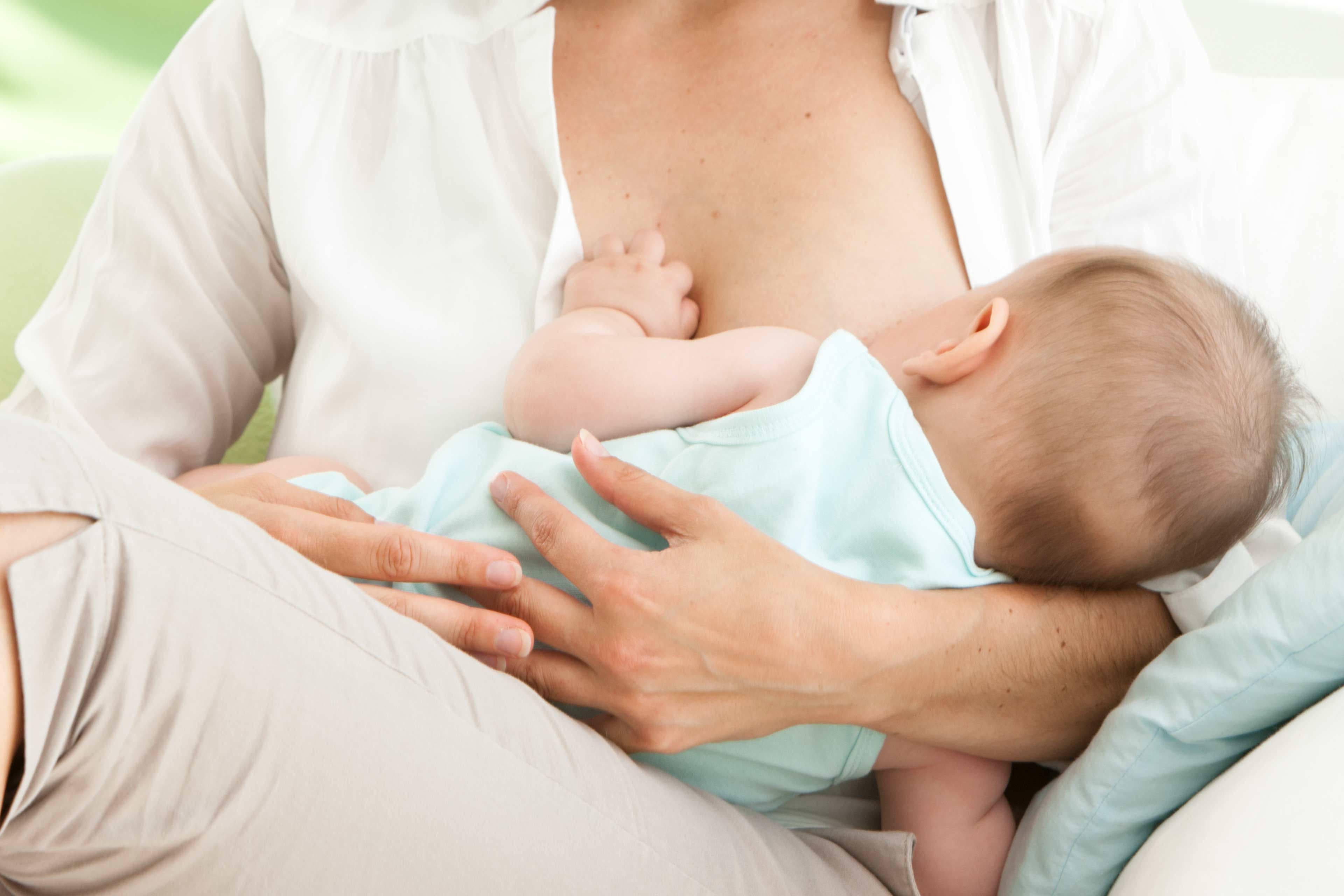 Stillende Mutter hält ihr Baby im Arm und legt es sanft an die Brust bei Milcheinschuss