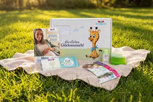 Produktpaket von HiPP Baby Club mit Broschüren, Produktproben, Milchportionierer und Geschenkbox auf einer Decke im Gras