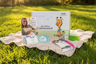 Produktpaket von HiPP Baby Club mit Broschüren, Produktproben, Milchportionierer und Geschenkbox auf einer Decke im Gras