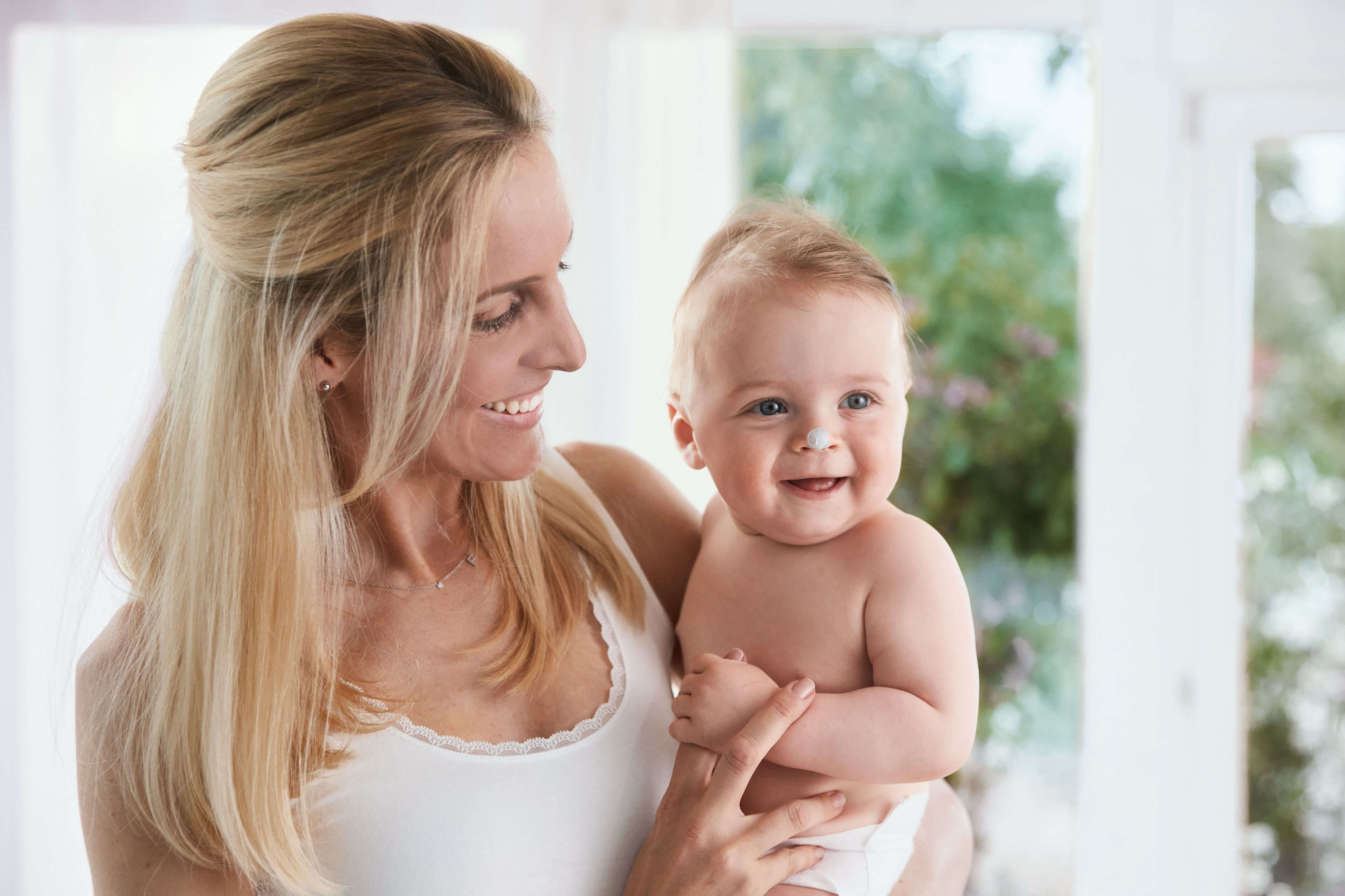 Eine Frau und ein Baby, beide lächelnd, wobei die Frau das Baby eng an sich drückt.