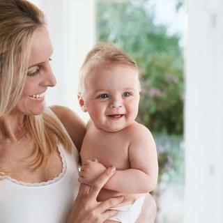 Eine Frau und ein Baby, beide lächelnd, wobei die Frau das Baby eng an sich drückt.
