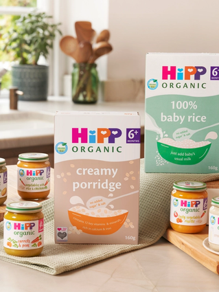 Selection of HiPP Organic baby foods and cereals arranged in a cosy kitchen, ready for starting baby on solid foods.