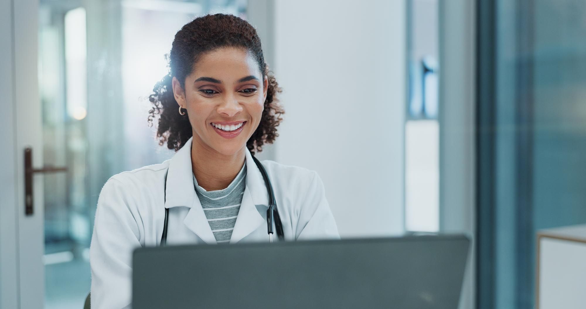 Female healthcare professional sat at a computer smiling in a clinical environment