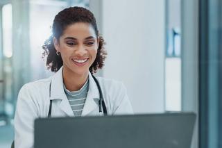 Female healthcare professional sat at a computer smiling in a clinical environment