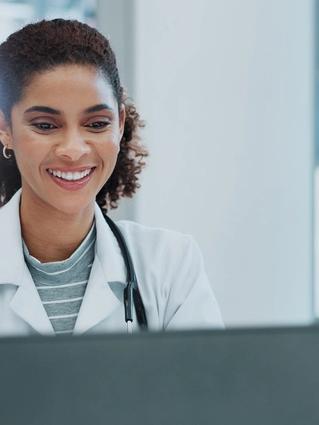 Healthcare professional sitting and smiling at her laptop