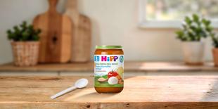 HiPP Bio Vegetarisches Menü Bunter Kartoffel-Auflauf im Glas mit Löffel auf Holztisch in heller Familienküche