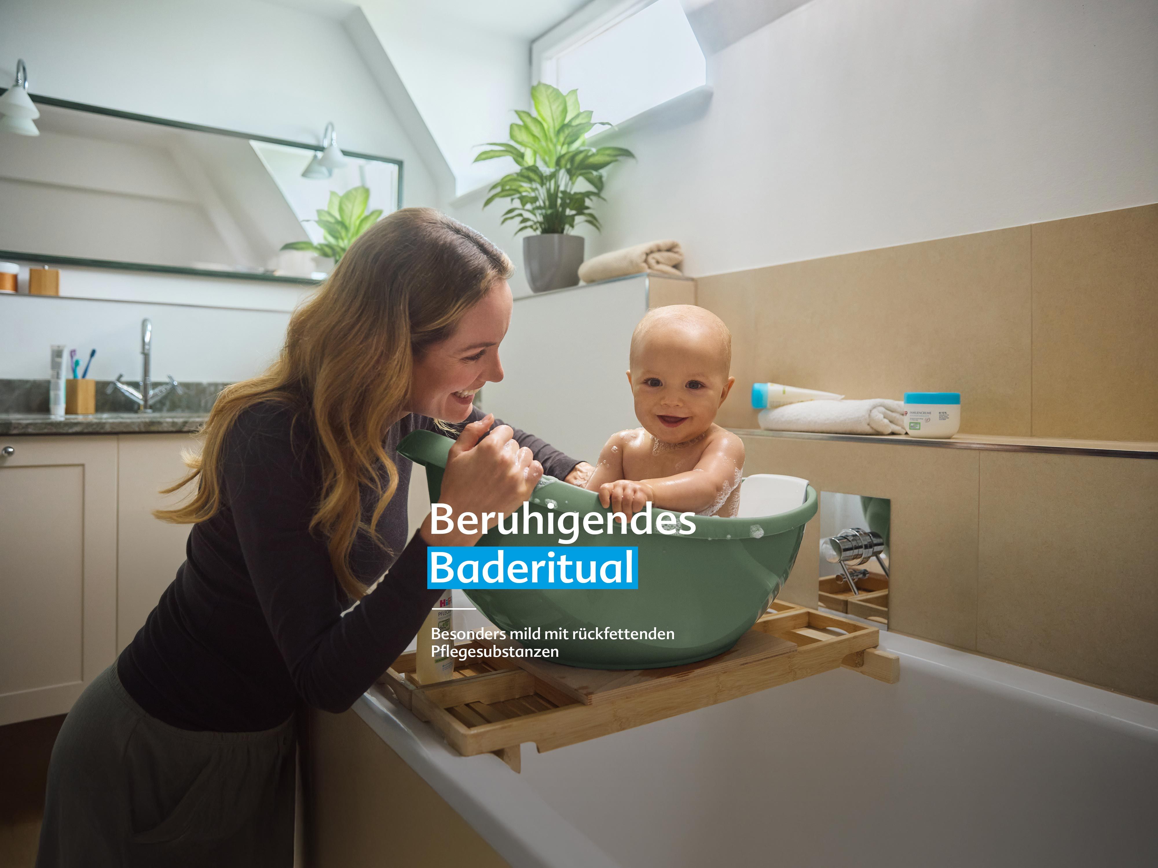Mutter badet ihr lachendes Baby in einer kleinen Wanne, Text „Beruhigendes Baderitual – besonders mild mit rückfettenden Pflegesubstanzen“.