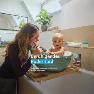Mutter badet ihr lachendes Baby in einer kleinen Wanne, Text „Beruhigendes Baderitual – besonders mild mit rückfettenden Pflegesubstanzen“.