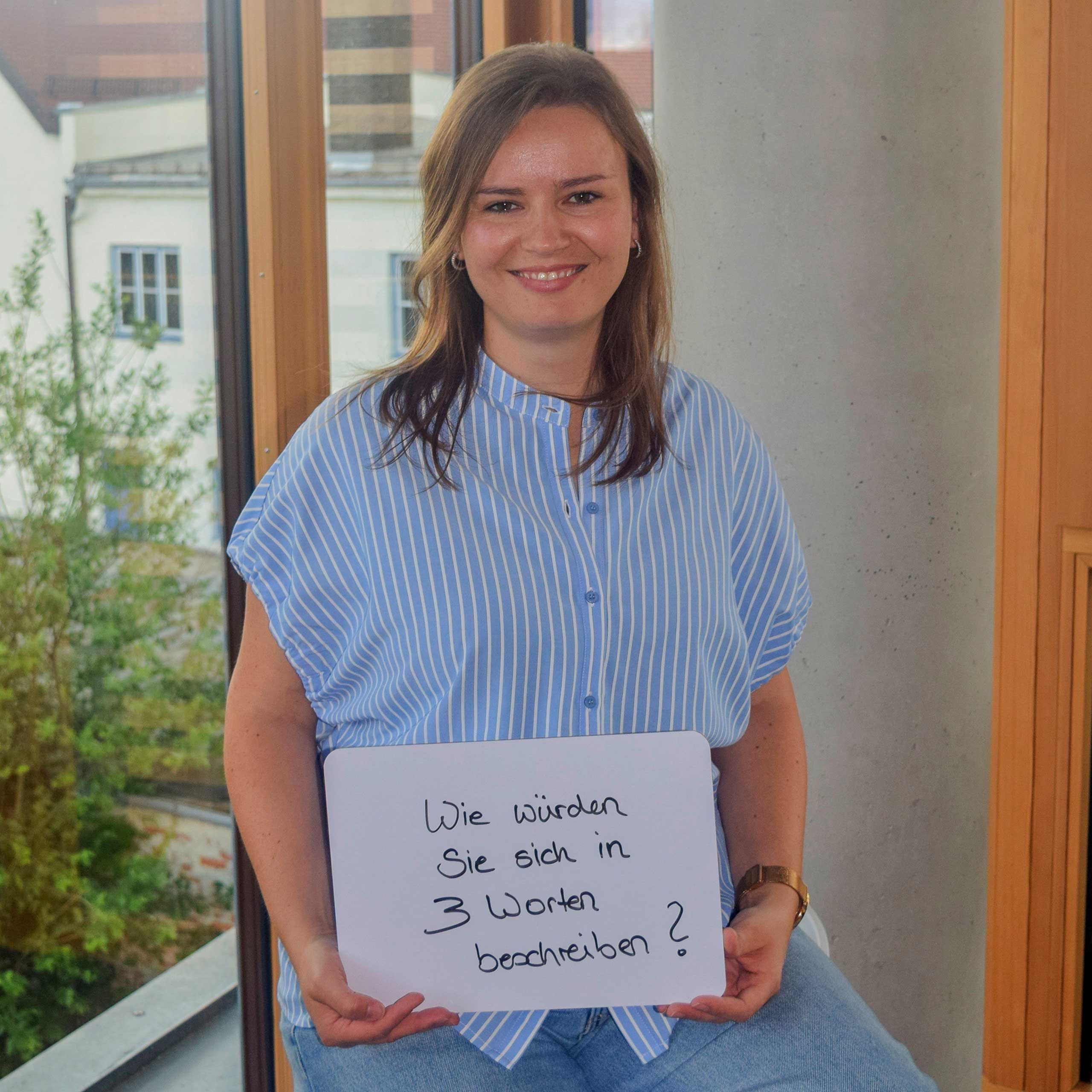 Eine HiPP Mitarbeiterin hält Schild mit der Aufschrift 'Wie würden Sie sich in 3 Worten beschreiben'