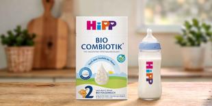 HiPP 2 BIO COMBIOTIK® Folgemilch-Packung und gefülltes Babyfläschchen auf Holztisch in heller Küche