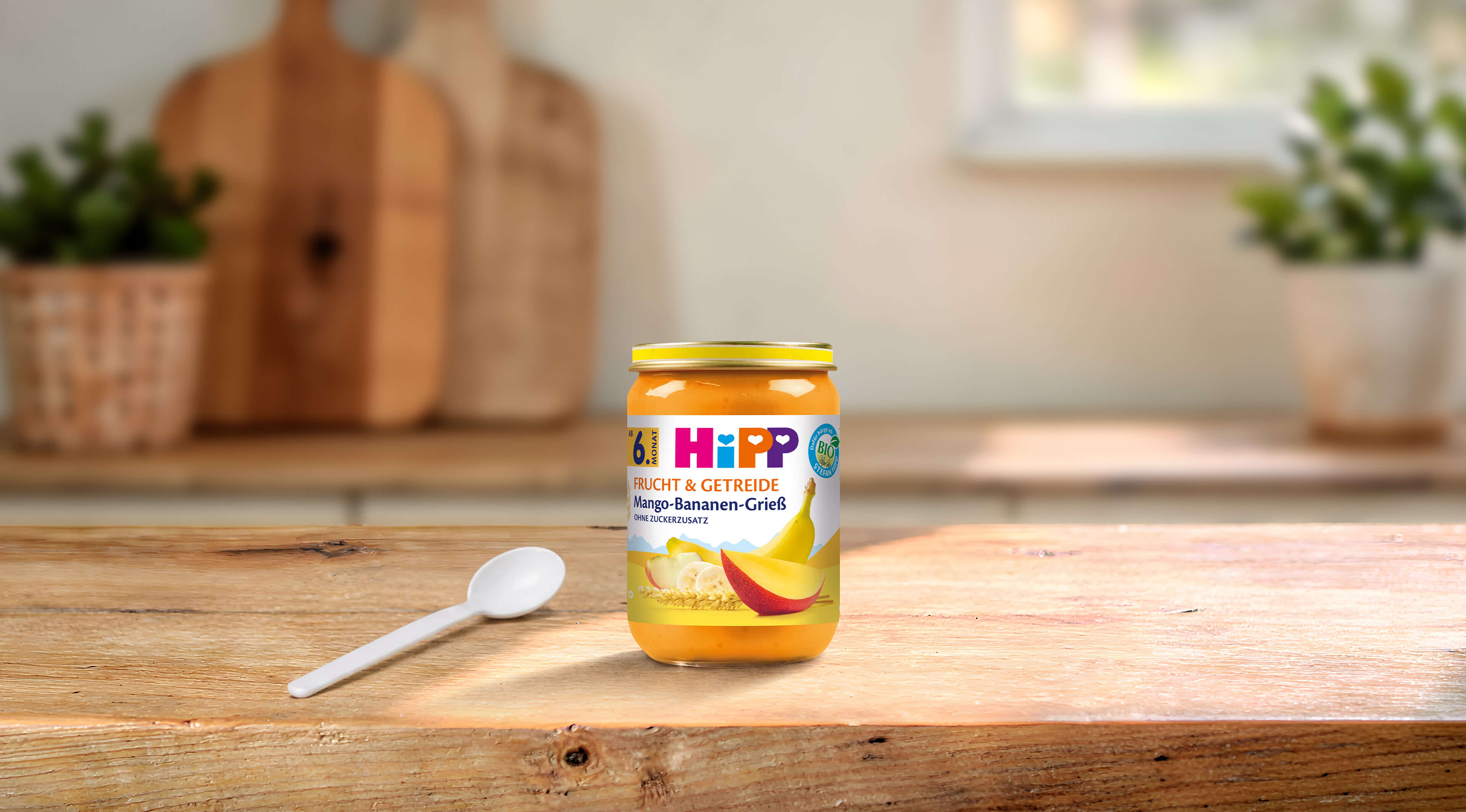 HiPP Bio Frucht & Getreide Mango-Bananen-Grieß 190g Glas auf Holztisch mit Löffel in heller Küche