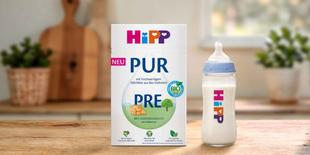 HiPP PRE PUR Bio-Anfangsmilch-Packung und gefülltes Fläschchen auf Holztisch in heller, gemütlicher Küche.