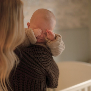 Baby rubbing eyes from crying over mums shoulder