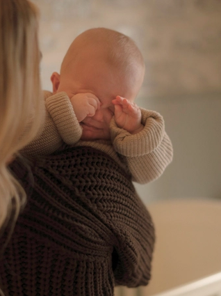 Baby rubbing eyes from crying over mums shoulder