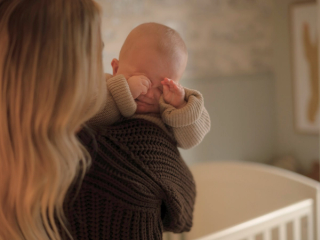 Baby rubbing eyes from crying over mums shoulder