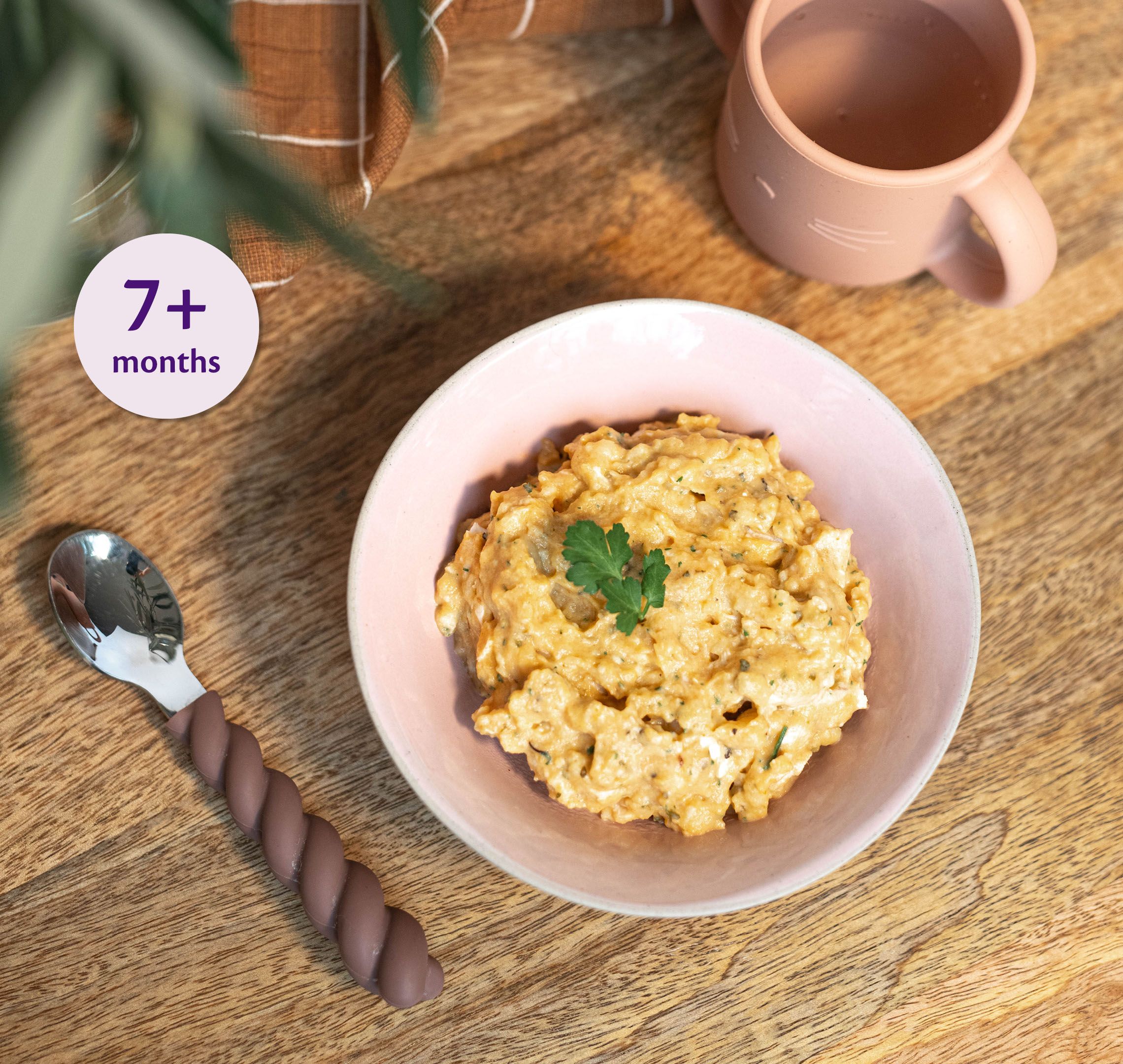 Bowl of creamy chicken and squash porridge for babies 7+ months, on a wooden table with baby spoon and cup nearby