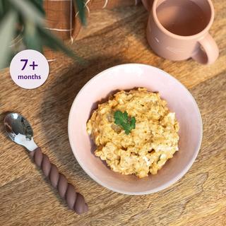 Bowl of creamy chicken and squash porridge for babies 7+ months, on a wooden table with baby spoon and cup nearby