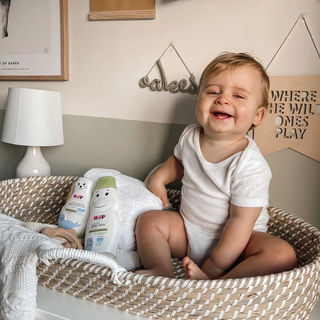 Baby sat in a Moses basket next to HiPP baby care bath products