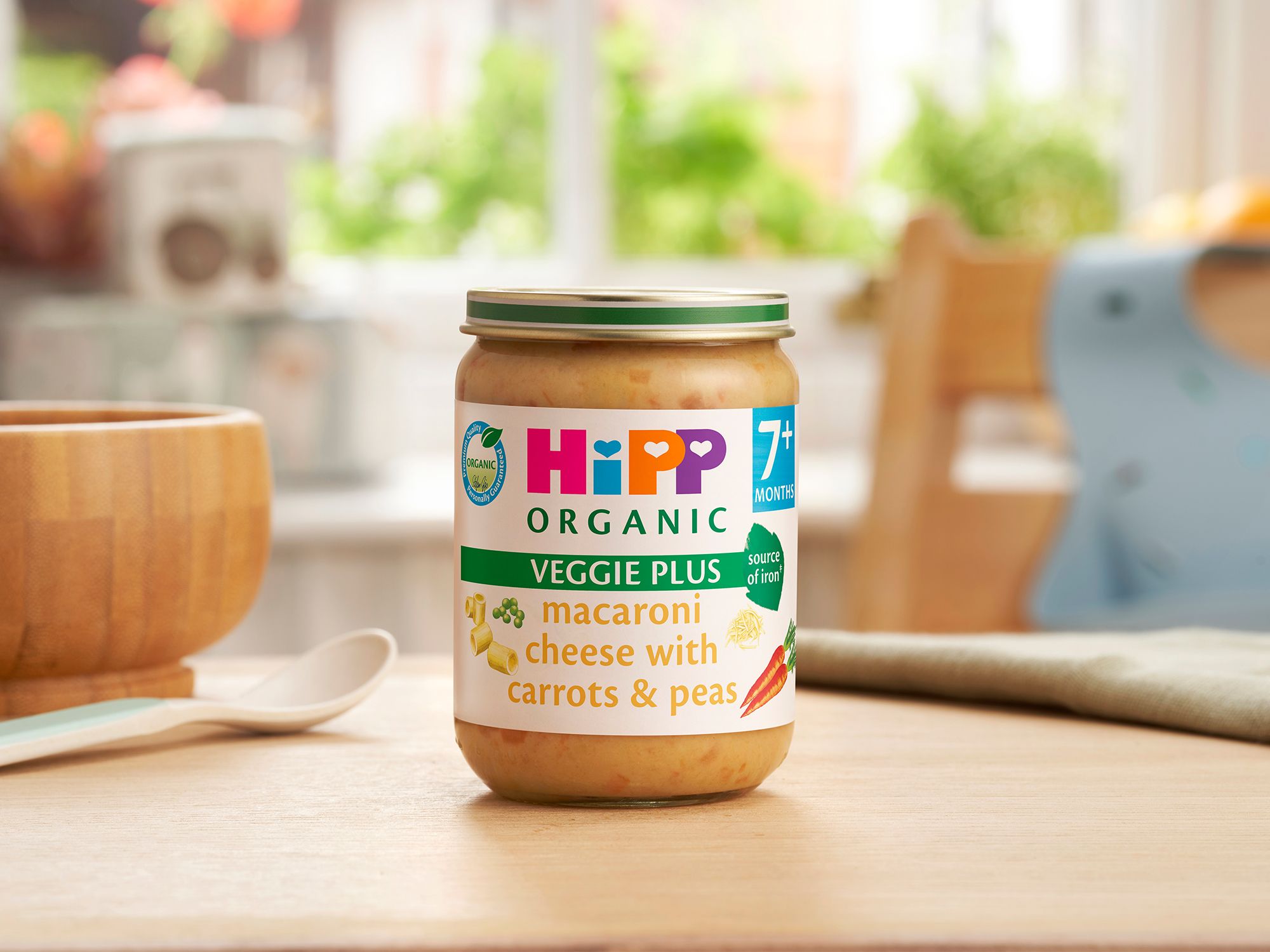 HiPP Organic Macaroni Cheese With Carrots & Peas on a dining table next to a bowl and spoon