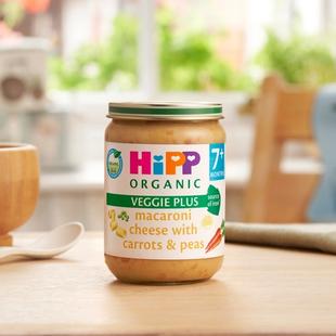 HiPP Organic Macaroni Cheese With Carrots & Peas on a dining table next to a bowl and spoon