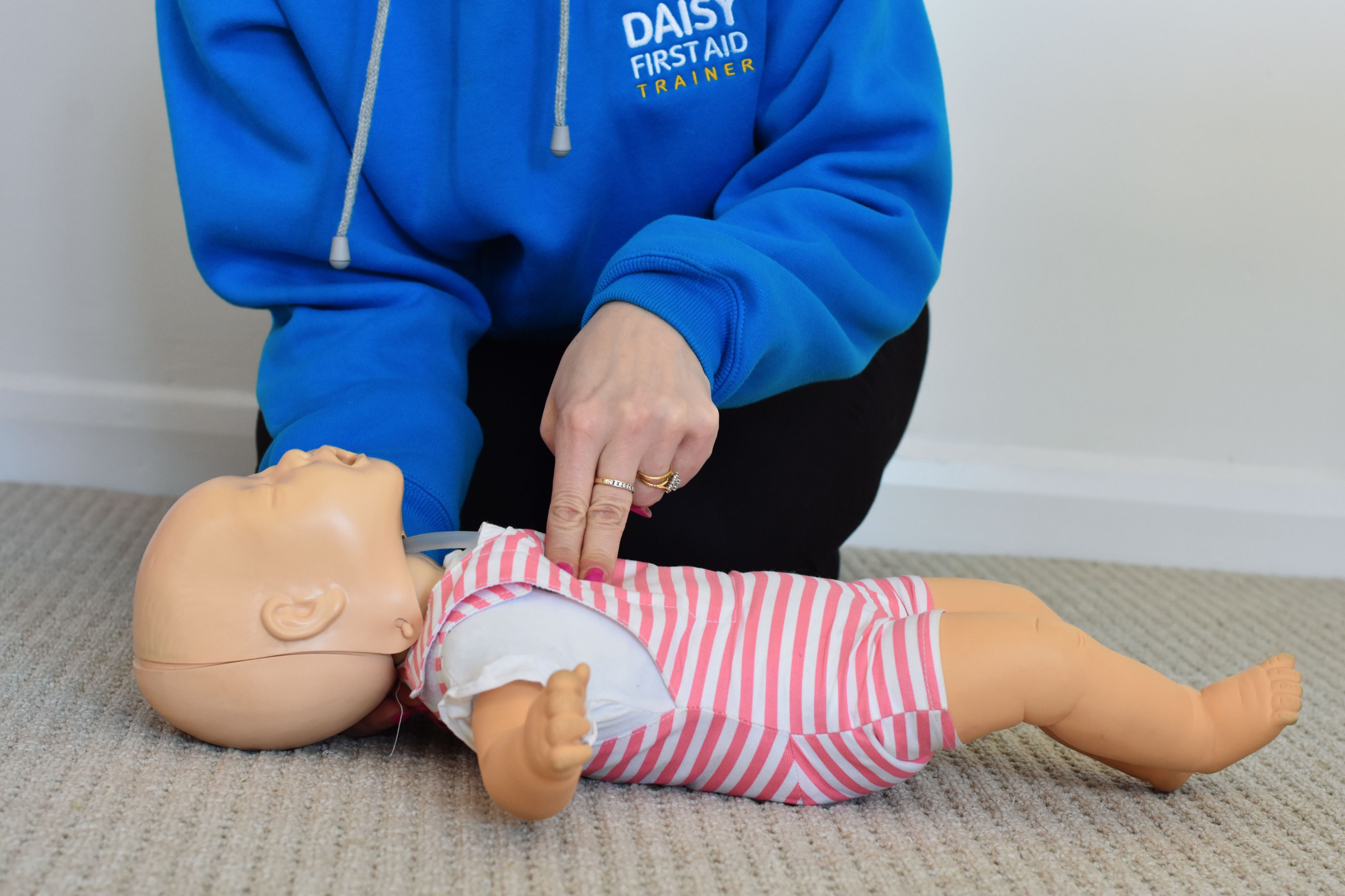Daisy First Aid trainer demonstrating baby CPR on an infant manikin lying on the floor