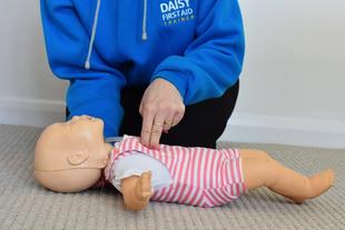 Daisy First Aid trainer demonstrating baby CPR on an infant manikin lying on the floor