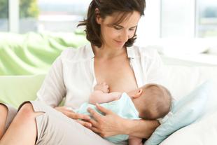 Eine Frau in einem weißen Hemd hält sanft ein Baby in einem hellblauen Outfit, während das Baby an ihrer Brust gestillt wird.