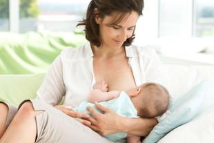 Eine Frau in einem weißen Hemd hält sanft ein Baby in einem hellblauen Outfit, während das Baby an ihrer Brust gestillt wird.