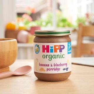 HiPP Organic Banana & Blueberry Porridge Jar on a dining table next to a bowl and spoon