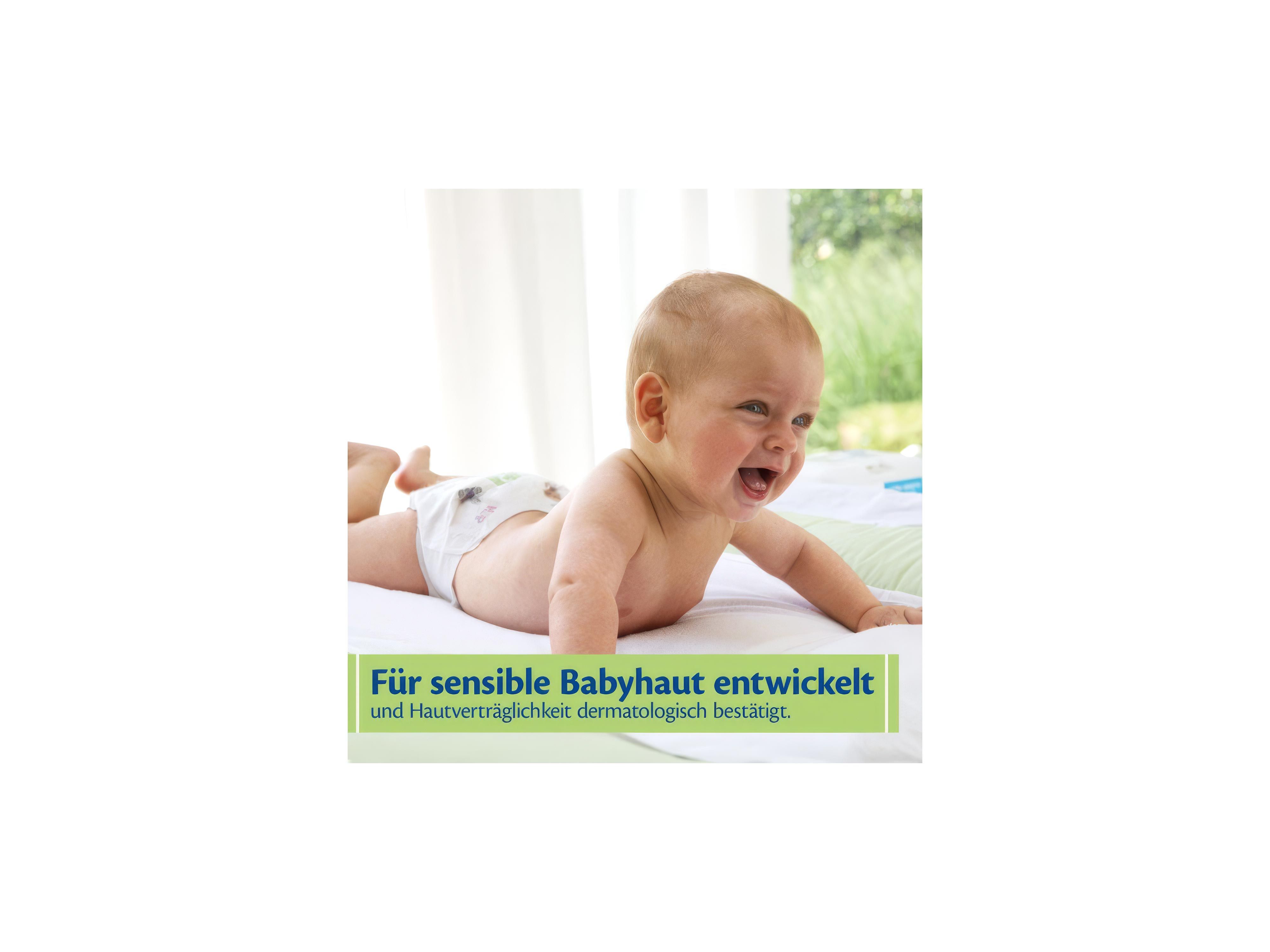 Ein Baby liegt auf dem Bauch auf einer weißen Unterlage und lächelt. Das Baby trägt eine Windel. Im Hintergrund sind unscharfe grüne Pflanzen und ein Fenster zu erkennen. Im unteren Bereich befindet sich ein gelb-grüner Kasten mit blauem und grünem Text.