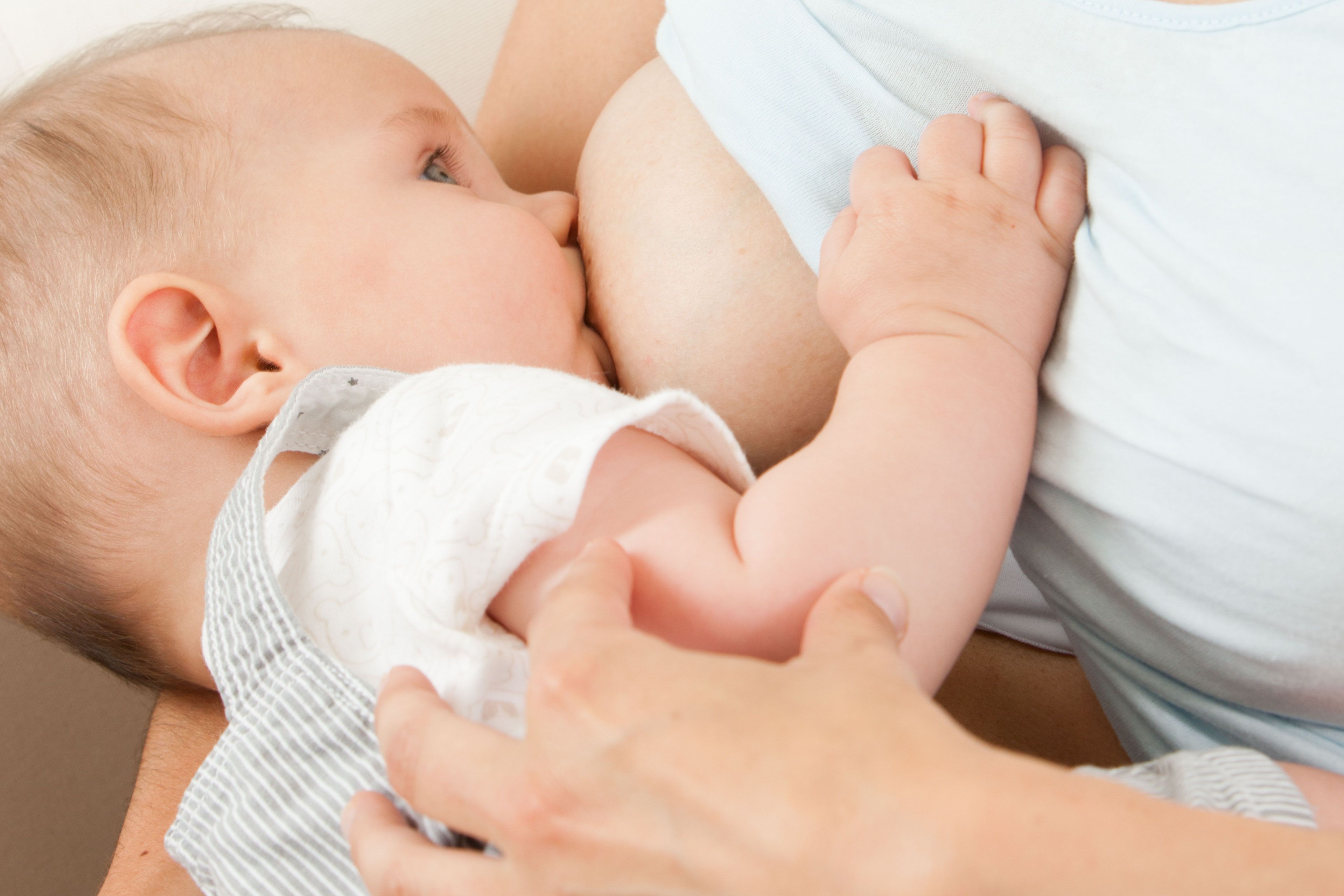 Ein Baby, das scheinbar gestillt wird, mit einer Nahaufnahme seines Gesichts und der Hand der Mutter.