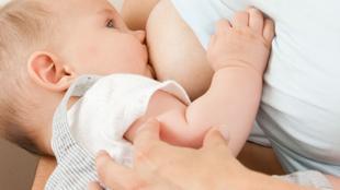 Ein Baby, das scheinbar gestillt wird, mit einer Nahaufnahme seines Gesichts und der Hand der Mutter.