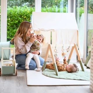 Mum playing with her toddler whilst her baby is on play amt