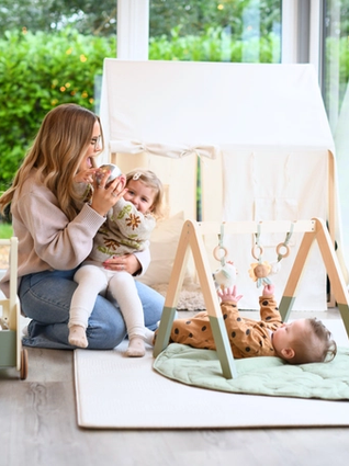 Mum playing with her toddler whilst her baby is on play amt