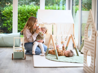 Mum playing with her toddler whilst her baby is on play amt