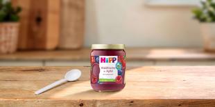 HiPP Bio-Gläschen „Waldfrüchte in Apfel“ ab 5. Monat auf Holztisch, daneben ein kleiner Löffel in heller Küchenumgebung
