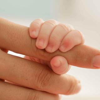 Die Hand eines Babys, die den Finger eines Erwachsenen ergreift, symbolisiert die Verbindung zwischen den Generationen.