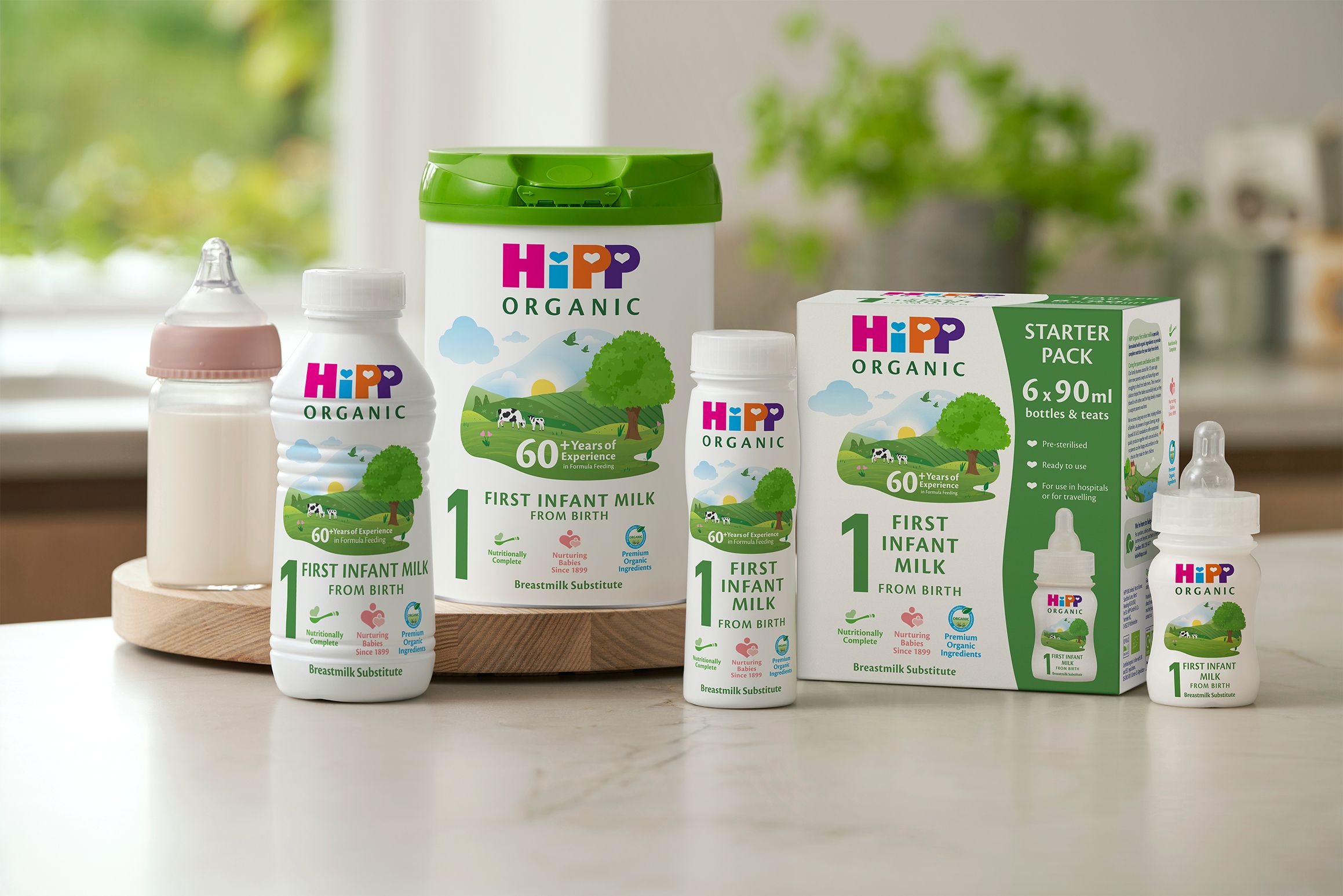 HiPP Organic First Infant Milk range, including powder tin, ready-made bottles and starter pack, arranged on a kitchen worktop