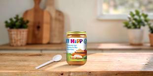 HiPP Bio-Gläschen Couscous mit Gemüse & Bio-Hühnchen ab 8. Monat auf Holztisch mit Löffel in heller Küche