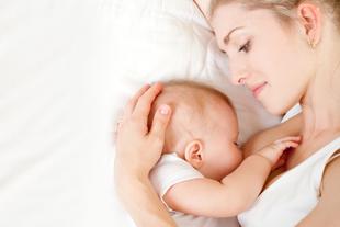 Ein zärtlicher Moment zwischen einer Mutter und ihrem Baby, in dem die Mutter das Baby sanft an sich drückt, während beide auf einer weißen Fläche ruhen.