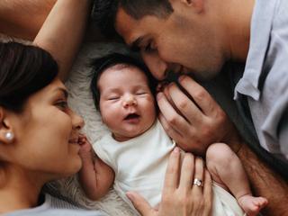 Eltern liegen mit Baby auf weichem Untergrund und berühren sich sanft