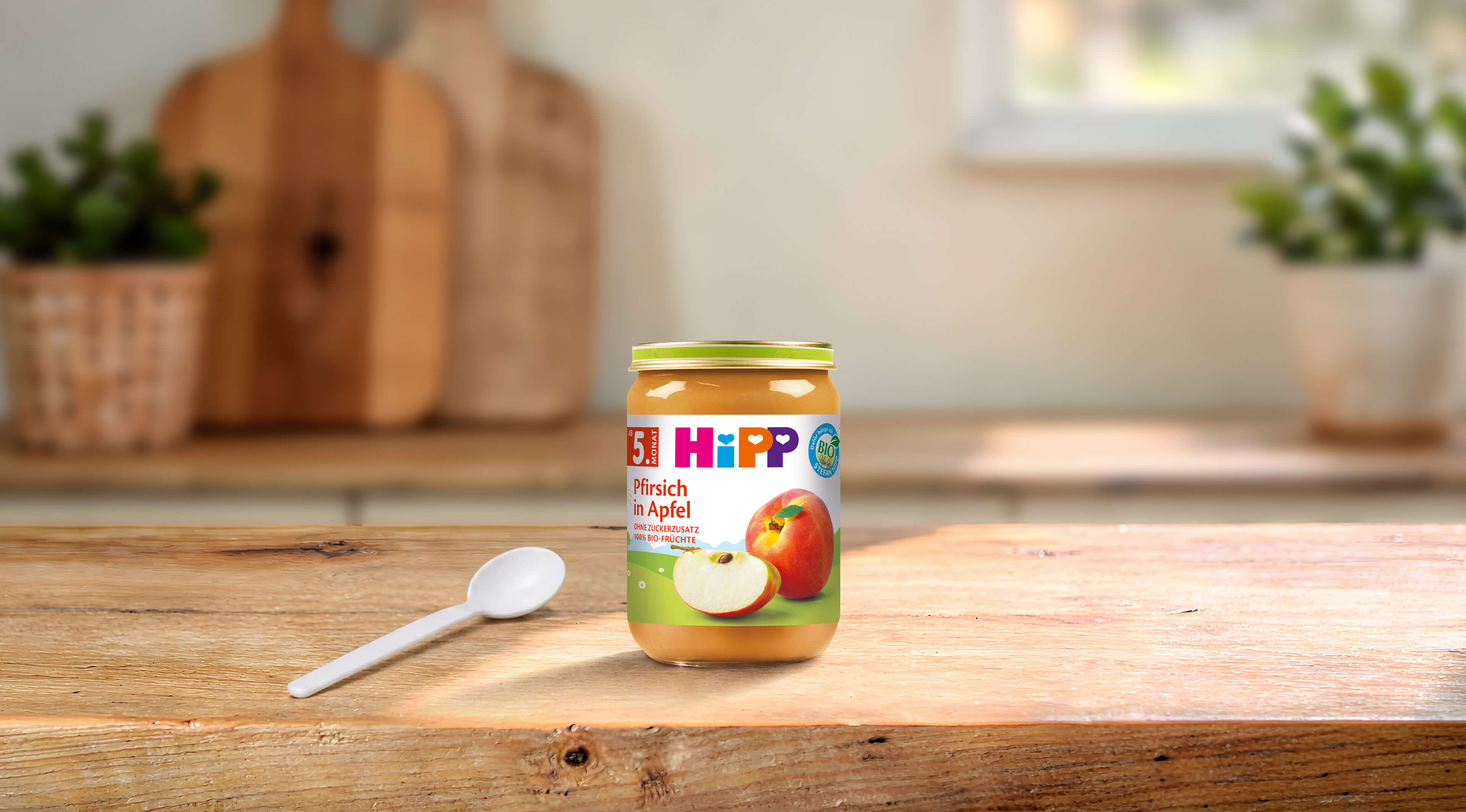 HiPP Bio Babygläschen Pfirsich in Apfel 190g auf Holztisch mit Löffel in heller Küchenumgebung